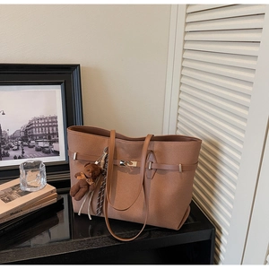 Detail of brown faux suede tote bag featuring a leather strap with metal buckle and bear charm