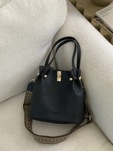 Winter black lychee leather bucket bag with woven strap shown on a beige sofa