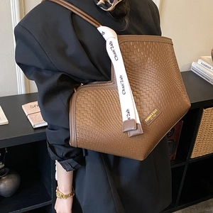 Detail of coffee woven tote bag featuring a decorative letter ribbon and logo patch