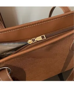 Detail of golden polished metal zipper on brown leather and canvas shoulder bag