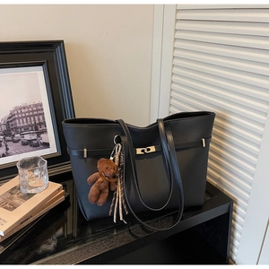 Detail of black matte tote bag with stitching, gold hardware and brown bear charm