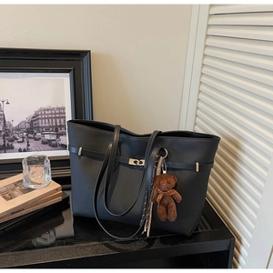 Detail of black faux leather tote bag featuring a gold buckle and brown plush bear charm