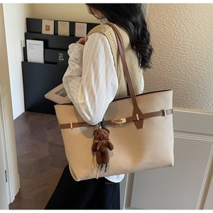 Detail of a beige tote bag with brown straps and a cute plush bear charm in a home setting