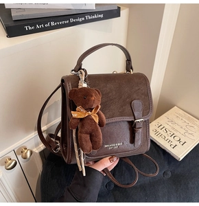 Close-up of vintage brown leather handbag with buckle strap and cute plush bear charm