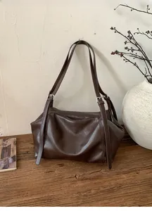 Detailed close-up of dark brown hobo tote bag with adjustable straps on a wooden surface