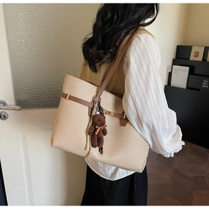 Detail of beige tote bag with brown leather straps and a cute plush bear charm