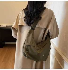 Vue arrière d'un sac bandoulière croissant en nylon vert olive porté avec un trench beige