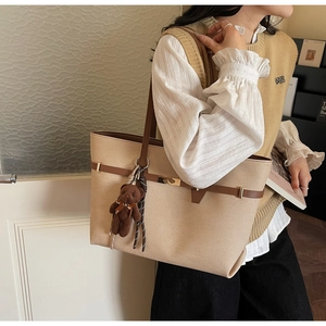 Detail of beige tote bag with brown straps and cute teddy bear charm hanging on side