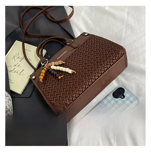 Detail of dark brown handbag featuring woven texture and beaded tassel charm