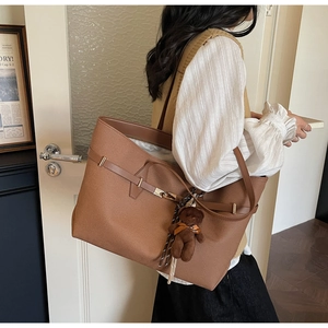 Close-up of brown leather tote bag with lychee texture and cute plush bear charm decoration
