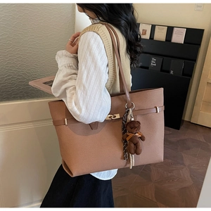 Detail of a large brown leather tote bag with metal twist buckle and cute plush bear charm
