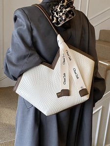 White woven tote bag with brown leather trim and V-cut top edge shown on shoulder