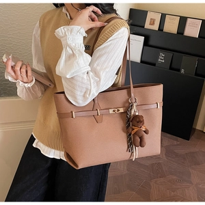 Close-up of a large brown tote bag with decorative buckle and cute bear pendant