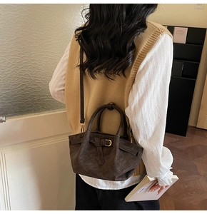 Détail du sac seau marron foncé en cuir matelassé porté par un mannequin en tenue chic