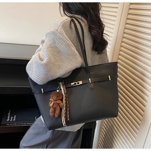 Detail of black tote bag with metal buckle and brown bear charm on shoulder