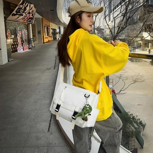 Detailed view of white nylon messenger bag with green dinosaur plush charm on strap