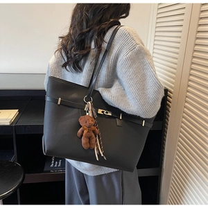 Detail of large black matte leather tote bag featuring a cute plush bear pendant accessory