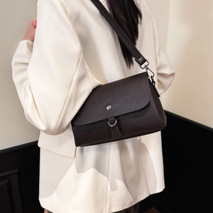 Detail of a dark leather crossbody bag with silver D-ring and metal stud closure