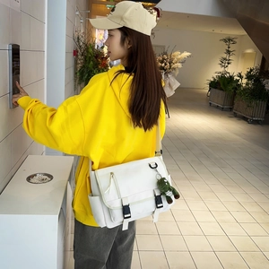White large capacity messenger bag with green dinosaur charm shown on a casual model