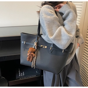 Detail of black textured leather tote bag featuring a silver twist lock and bear charm
