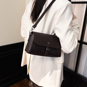 Detail view of a dark brown leather crossbody bag featuring a round metal buckle closure
