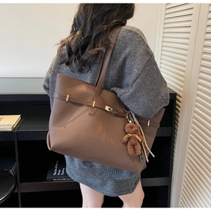 Brown faux leather tote bag with decorative metal buckle and plush bear charm detail