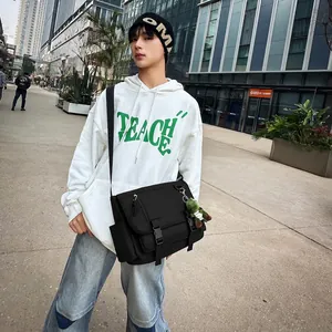 Street style view of a black multi-pocket crossbody bag with green dinosaur pendant