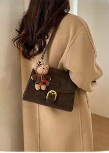 Model wearing a vintage dark brown crossbody bag with gold buckle and a cute bear charm