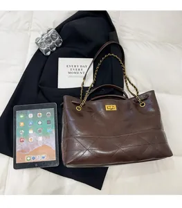Detail of dark brown quilted leather bag with gold clasp and chain strap on bed