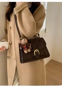 Detail of vintage brown suede crossbody bag with gold buckle and cute bear charm
