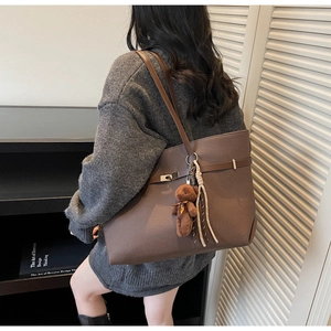 Detail of a large brown tote bag featuring decorative buckles and a plush bear pendant