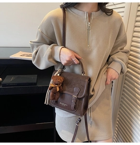 Detail of vintage brown crossbody bag with plush bear charm and beige knit dress
