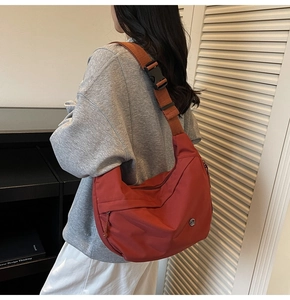 Détail du sac bandoulière en nylon rouge avec large sangle et logo métallique