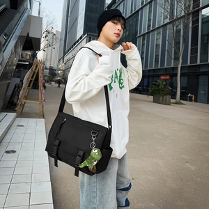 Detail of waterproof black messenger bag with green dinosaur plush keychain on city street