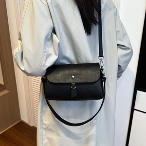 Detail showing the black leather crossbody bag texture and decorative circular ring