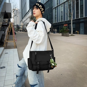 Detail view of black canvas crossbody bag with metal buckle and green plush dinosaur charm