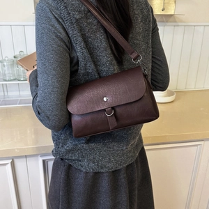Detail view of the vintage leather texture and metallic ring clasp on a brown crossbody bag