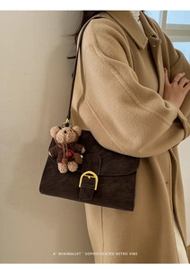 Detail of dark brown vintage shoulder bag with gold D-buckle and bear charm on camel coat