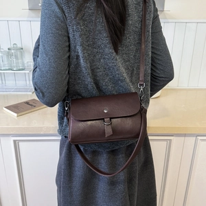 Detail of a dark brown leather crossbody bag styled on a model in a retro setting