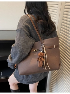 Brown large capacity tote bag with bear charm and tassel shown on model shoulder