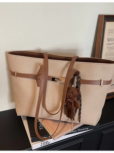 Large beige canvas tote bag with brown leather straps and a plush bear charm on books