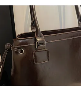 Macro view of glossy oil-wax leather texture and silver metal hardware on a tote bag