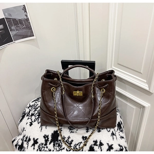 Détail d'un sac cabas marron foncé matelassé avec fermoir doré et bandoulière en chaîne