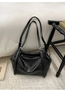 Detail of minimalist black leather tote bag with silver buckles and retro textured finish