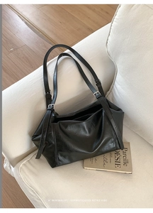 Grand sac cabas noir minimaliste avec bandoulières réglables posé sur un canapé chic