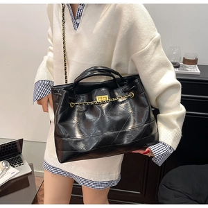 Detailed view of black quilted faux leather tote bag with chain strap and twist lock