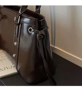 Detail of dark brown glossy leather tote bag with silver rivets and knotted cord side design