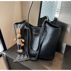 Detail of a black leather tote bag featuring a cute plush rabbit charm and lettered print