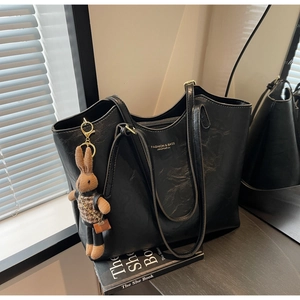 Macro detail of black leather tote bag featuring a cute bunny pendant and logo lettering