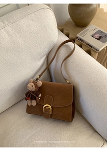 Detail of retro brown crossbody bag with gold buckle and cute bear charm on a sofa